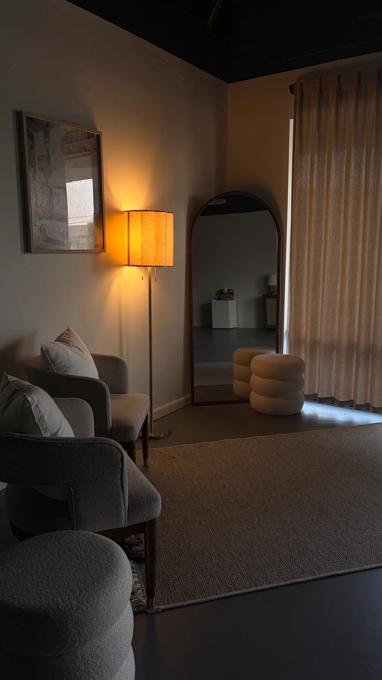 A warm, low-lit lounge corner at Embodi Mat Pilates with bouclé chairs, a floor lamp, and an arched mirror.